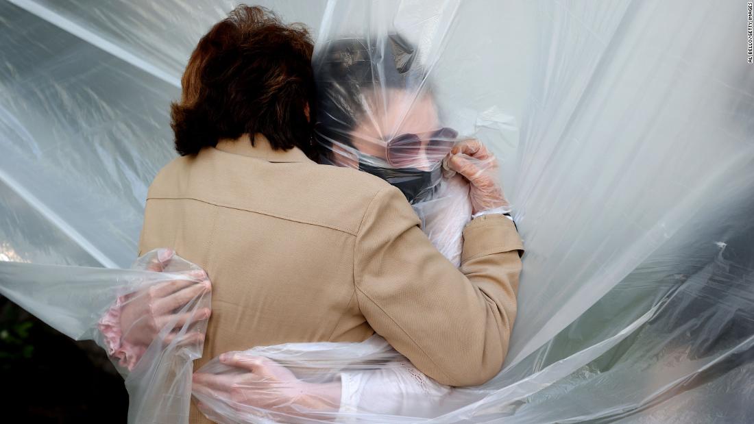 Olivia Grant, right, hugs her grandmother, Mary Grace Sileo, through a plastic drop cloth that was hung up on a homemade clothesline in Wantagh, New York, on May 24.